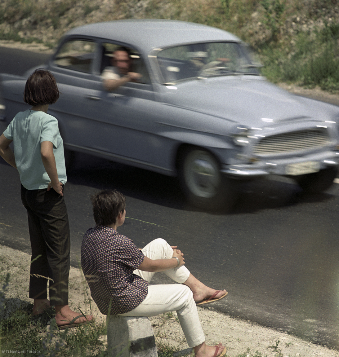 Magyarország, 1964. június 14. Fiatalok várakoznak a balatoni országút mellett, hogy egy gépkocsi felvegye őket és eljuthassanak úti céljukhoz. A felvétel készítésének pontos helye ismeretlen.