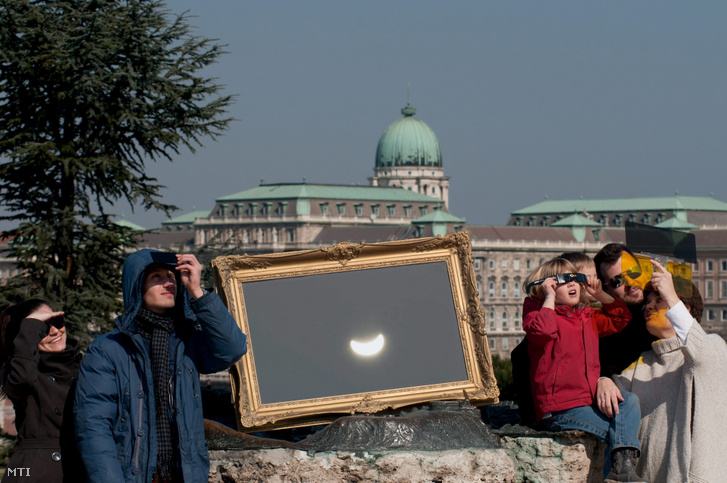 A kettős expozícióval készült felvételen érdeklődők nézik a részleges napfogyatkozást a fővárosi Gellért-hegyen 2015. március 20-án
