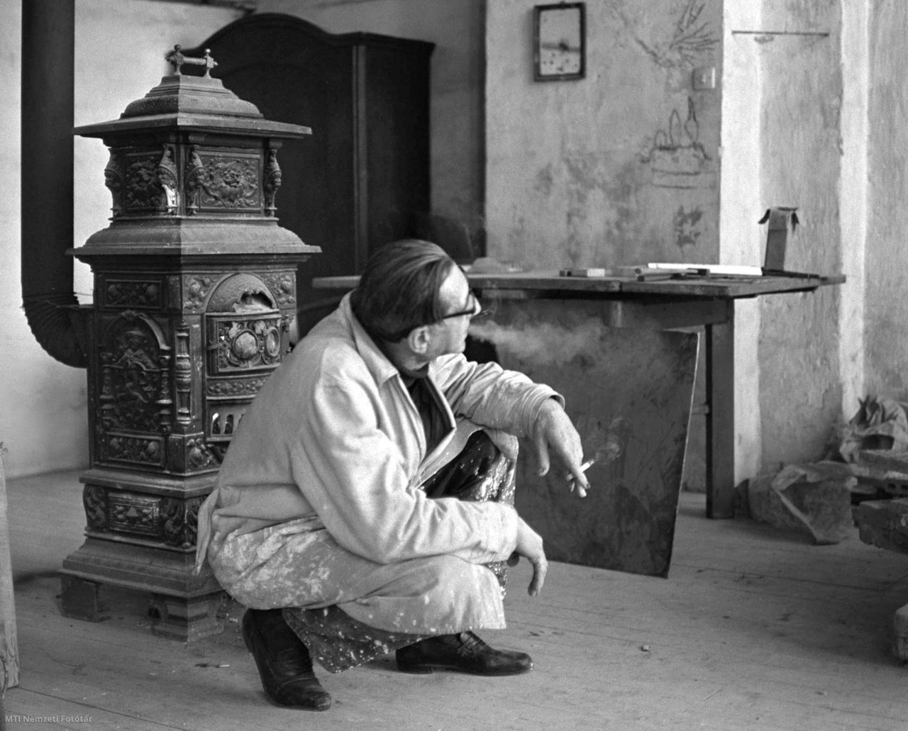 Budapest, 1967. január 4. Vilt Tibor szobrászművész műtermében a kályha előtt guggolva cigarettázik. A művész hozzákezdett a pályázati Madách Imre-szobor életnagyságú változatának megmintázásához. A szobrot bronzba öntve a Margitszigeten helyezik majd el