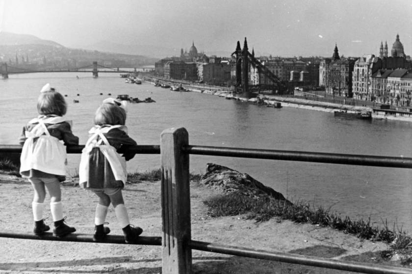 A fotó a háború után, 1951-ben készült. A Lánchíd munkálatai már befejeződtek, de az Erzsébet híd még romokban áll. A fotó erejéhez hozzájárul, hogy a látképet, melyen ott a pusztítás nyoma, két kicsi lány nézi.
