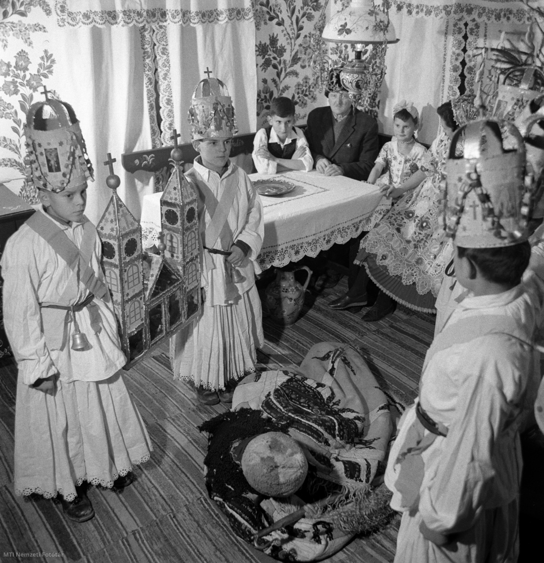 Kalocsa, 1965. december 23. Gyerekek betlehemeznek egy parasztházban. A betlehemezés a karácsonyhoz kötődő magyar népszokás, melynek középpontjában a betlehemi pásztorok párbeszédes, énekes játéka áll, Jézus születéséről szóló bibliai történet előadása. Fő kelléke a templom alakú betlehemi jászol, a Szent Családdal. Az előadás után a háziak megvendégelik őket.