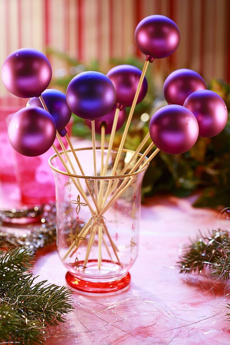 Néhány hurkapálca, és ugyanennyi lila színű gömbdísz szükséges ehhez az asztali dekorációhoz. Szúrd a tetejükbe, ahol az akasztó rész található, a pálcikákat, rögzítsd ragasztóval, majd rendezd őket egy áttetsző vázába.