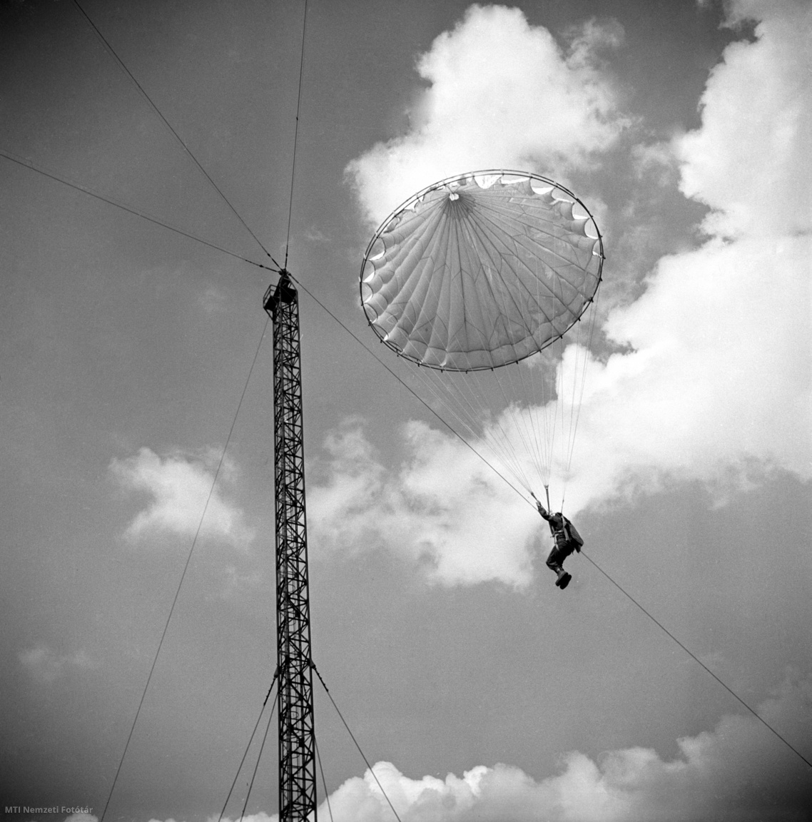 Budapest, 1954. június 17. Ejtőernyős toronyugró ereszkedik le a népligeti ugrótoronyból. A nyitott ejtőernyőt fémkeretre erősítik, ezzel együtt a torony tetejére húzzák, ahonnan az ernyő leoldása után ugrik le az ejtőernyős