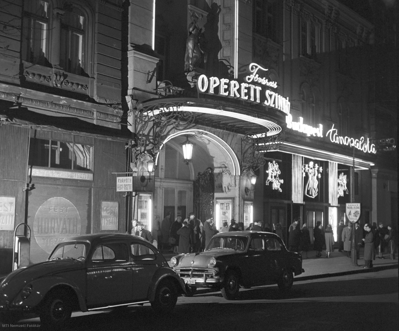 Budapest, 1960. december 23. Távozó vendégek az esti előadás végén a Fővárosi Operettszínházból. Az út szélén egy Volkswagen (b) és egy Moszkvics parkol. A háttérben a Budapest Táncpalota bejárata