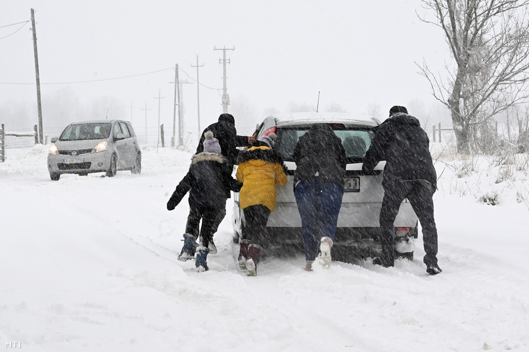 Egy havas úton elakadt autót tol egy család a Bakonyban, Tés határában.