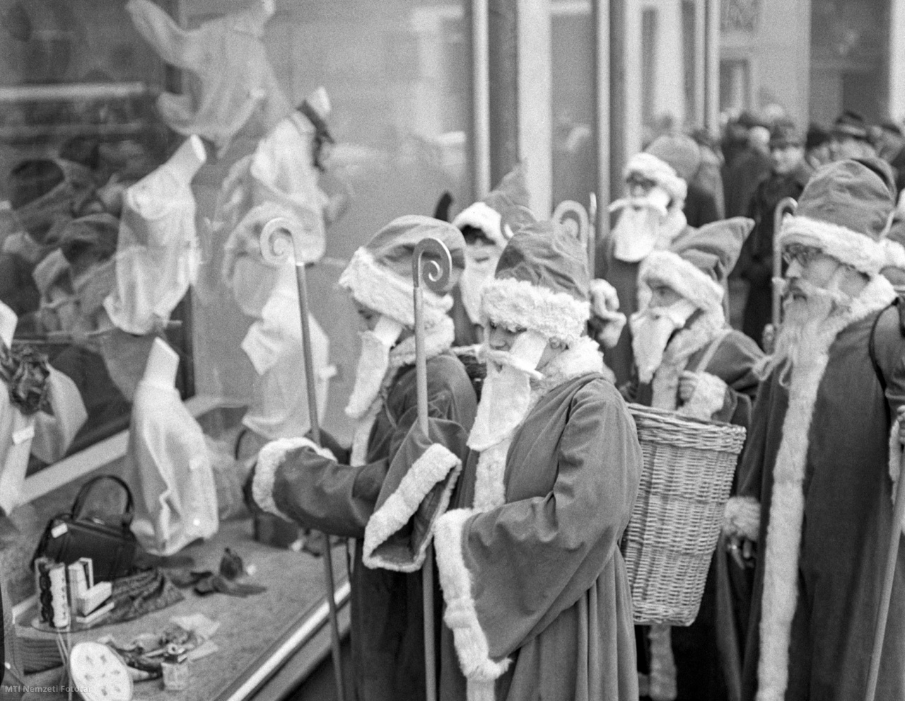Budapest, 1965. november 24. Télapójelmezbe öltözött emberek egy ruhaüzlet kirakatát nézik a belvárosban. Habár még egy hét van hátra a hagyományos téli ünnepek egyik ajándékozónapjához, a Mikulás december 6-i ünnepéhez, a Jelmezkölcsönző Vállalat ruhakellékeibe öltözve már megjelentek a télapók a főváros utcáin, hogy elsősorban a gyerekeknek majd ajándékokat adjanak