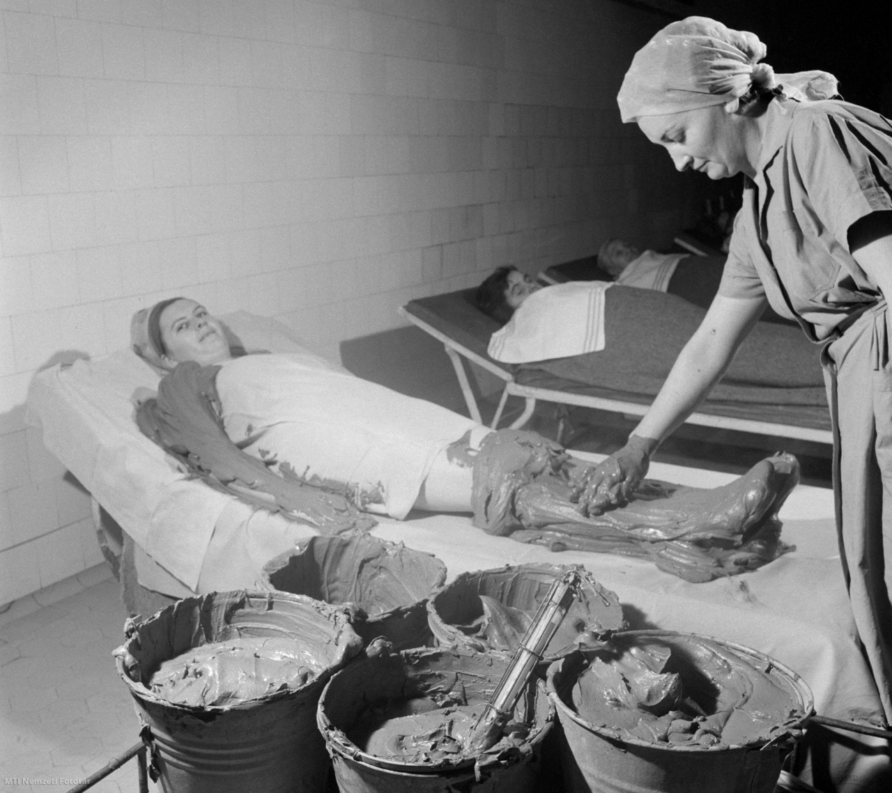 Budapest, 1965. november 25. Beteg iszappakolása az Országos Rheuma és Fürdőügyi Intézetben (ORFI). Hazánkban a reumatikus megbetegedések elleni gyógymódok nagy múltra tekintenek vissza. Világszerte ismertek a magyarországi gyógyfürdők, számosan nyerték már vissza egészségüket például az iszapkezelés segítségével. A hagyományos gyógymódokon kívül egyre nagyobb teret kapnak az elektromos és ultrahangos kezelések.