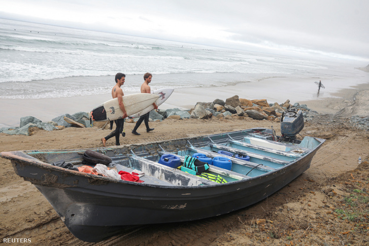 Szörfösök sétálnak egy halászhajó mellett, miután nyolc holttestet találtak a parton