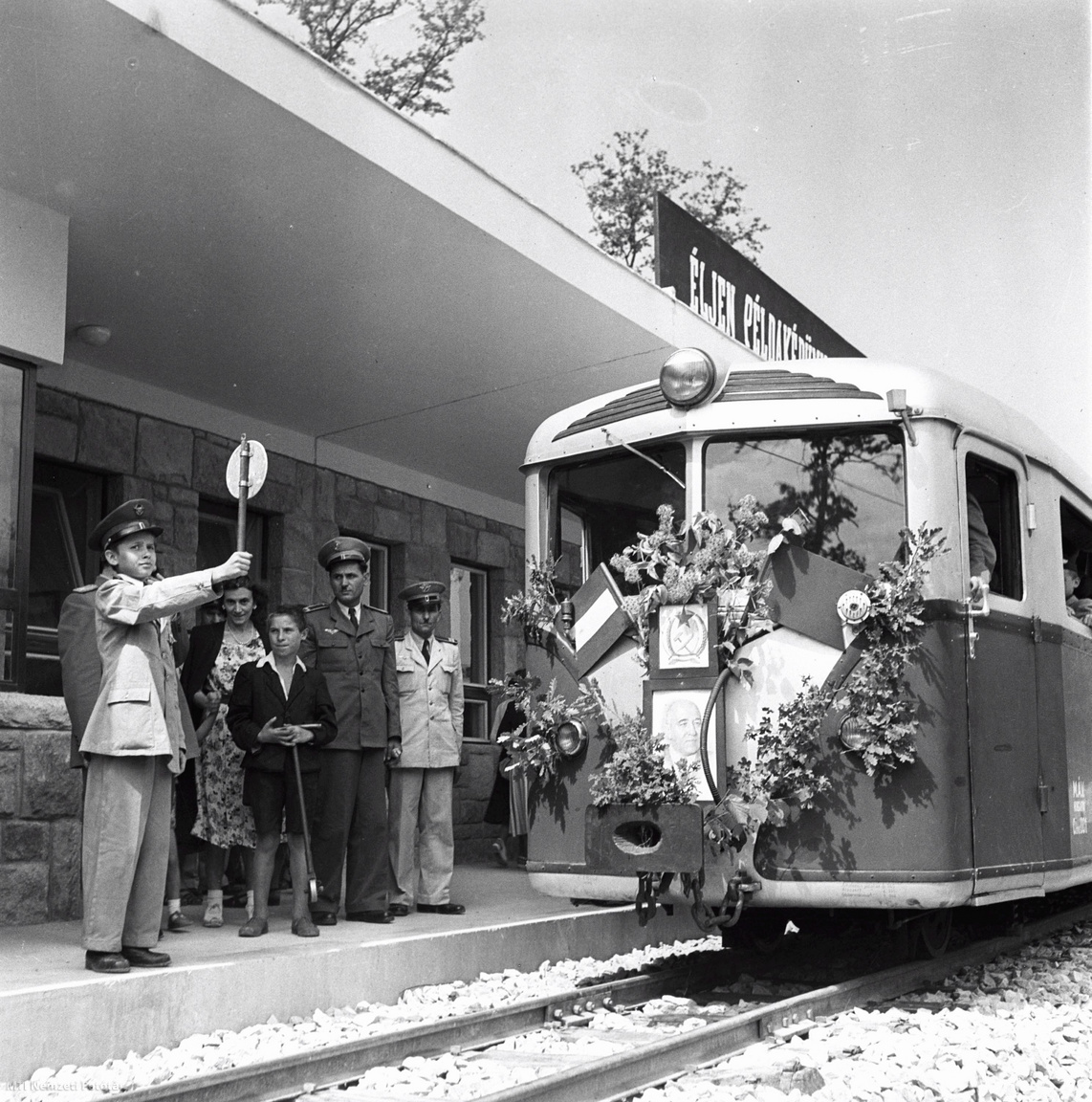 Az úttörővasutas jelzésére a feldíszített vonat elindul az új vonalon. 1948. július 31-én átadták a forgalomnak a Gyermekvasút első, 3,6 kilométeres, Széchenyi-hegy és Virágvölgy (akkori nevén Előre) állomás közötti szakaszát. Az Úttörővasút harmadik szakaszának avatóünnepségét 1950. augusztus 19-én tartották Hűvösvölgyben