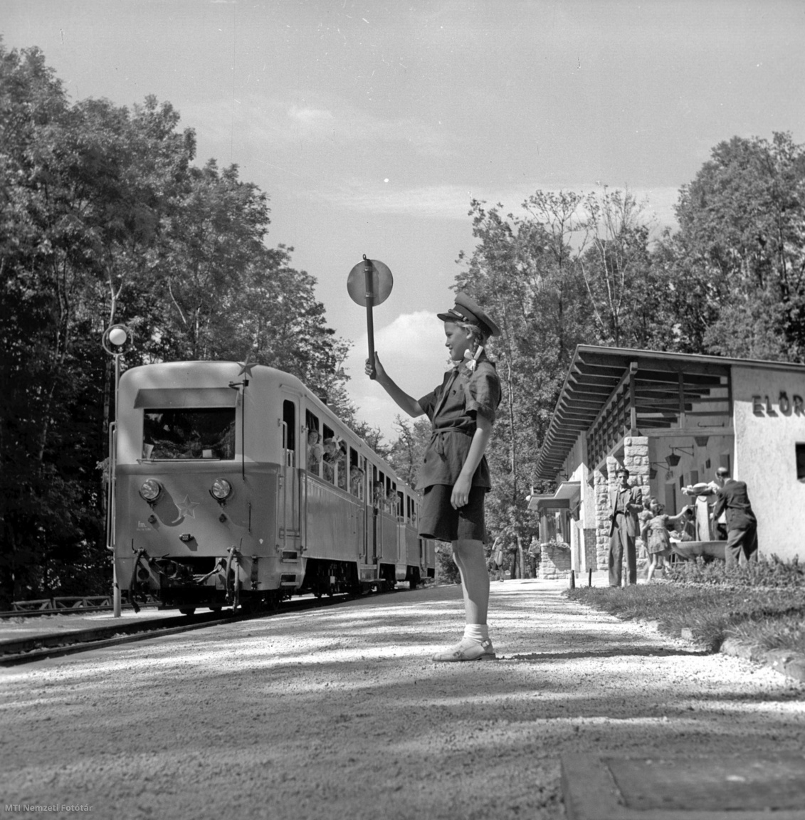 Budapest, 1954. augusztus 30. Az ügyeletes forgalmista lány a zöld tárcsa felmutatásával elindítja az Úttörővasút szerelvényét a Ságvári-ligeti Előre állomásról