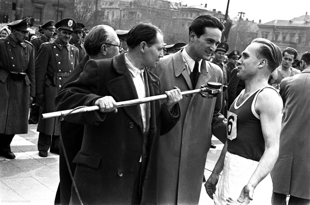 Budapest, 1947. március 30. Szepesi György sportriporter interjút készít a felszabadulási staféta egyik indulójával a Hősök terén. A hosszú nyélre szerelt mikrofont a rádió technikusa tartja.