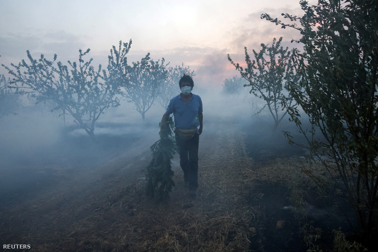 Egy férfi ágat visz a füstben, miközben erdőtűz ég a közép-görögországi Szeszklóban 2023