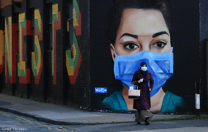 Egy maszkot viselő nő sétál egy NHS-munkást ábrázoló utcai műalkotás mellett Londonban 2020. április 21-én