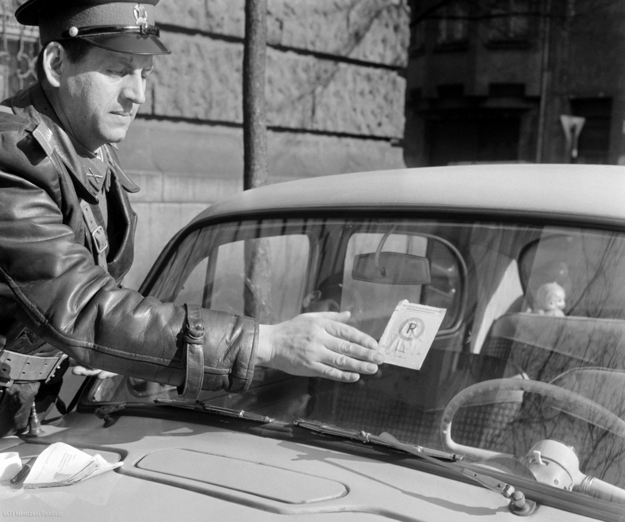 Budapest, 1964. február 18. A Közlekedési Rendőrség rendőre Parkírozni tilos feliratú figyelmeztető matricát ragaszt a szabálytalan helyen parkoló CB 93-16 rendszámú személyautó szélvédőjére. A matrica egyelőre még csak figyelmeztetés, de ha ugyanazon gépkocsivezető kocsijával többször találkoznak a tilosban, megbüntetik