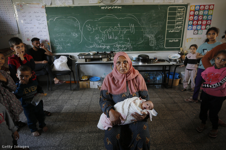 Egy lakóhelyét elhagyni kényszerült palesztin nő tart egy csecsemőt az ENSZ Palesztin Menekülteket Segélyező és Munkaközvetítő Hivatalának (UNRWA) iskolájában a gázai Deir al-Balahban, amelyet menedékhelyként használnak, miközben az izraeli légicsapások folytatódnak 2023. november 18-án