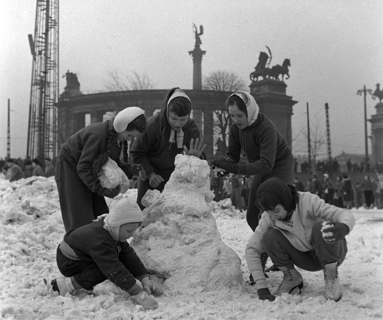 Budapest, 1960. december 31. Hóembert építő korcsolyázók a városligeti Műjégpálya területén. A háttérben a Hősök tere és a Millenniumi emlékmű jobb karéja.