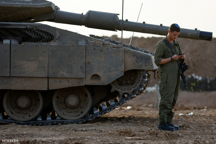 Egy izraeli katona mobiltelefont használ egy harckocsi mellett az izraeli-gázai határ közelében Dél-Izraelben 2023. november 26-án