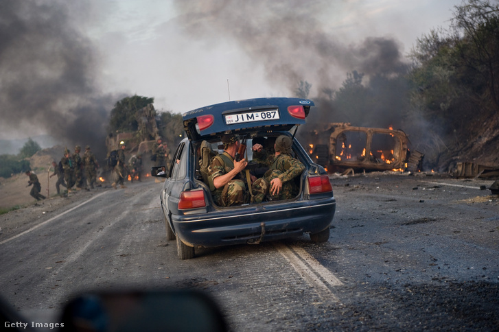 Grúz katonák ülnek egy civil járműben, miközben egy grúz páncélozott személyszállító jármű összetörve fekszik a Gori és Tbiliszi közötti úton, 2008. augusztus 11-én, a grúziai Gori közelében. Oroszország cáfolta azokat a híreket, amelyek szerint orosz csapatok nyomulnának Tbiliszi felé, mivel a térségben törékeny tűzszünet van érvényben