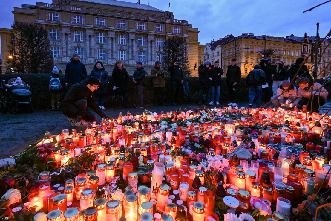Emberek gyászolnak az áldozatok ideiglenes emlékhelyénél a Prága központjában lévő Károly Egyetem előtt 2023. december 22-én, miközben a rendőrségi nyomozók tovább dolgoznak az egyetemen a halálos tömeges lövöldözést követő napon
