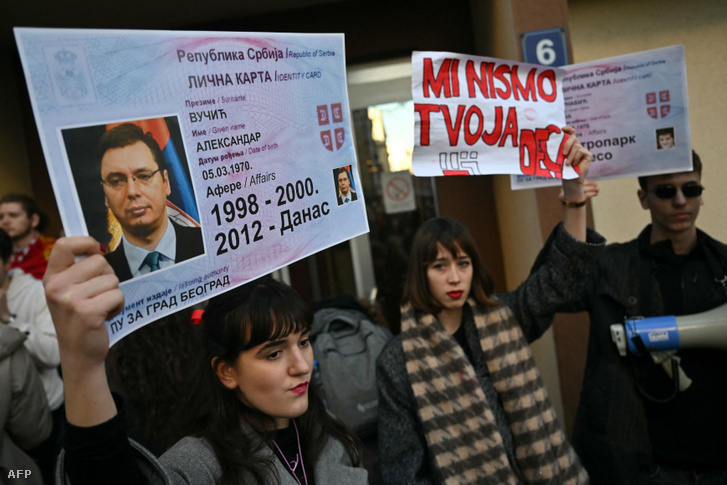 Egy diák Aleksandar Vucic személyi igazolványát ábrázoló plakátot tart, amint elzárják az utcát a Közigazgatási és Helyi Önkormányzati Minisztérium előtt Belgrádban 2023. december 25-én
