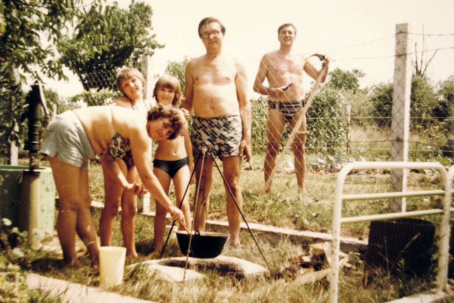 Családi bográcsozás a telken fürdőruhában, a háttérben a szomszéd a kaszával. Egy klasszikus idilli pillanat a gulyáskommunizmus utolsó évtizedéből.