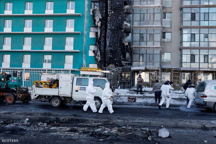 Védőfelszerelést viselő szakemberek sétálnak egy robbanás által megrongált épülethez, miután egy cseppfolyósított földgázt szállító teherautó felrobbant Ulánbátorban, Mongóliában 2024. január 24-én