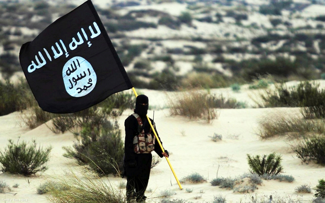 Az Iszlám Állam maszkos katonája az Iszlám Állam zászlóját tartja valahol Irak vagy Szíria sivatagában, 2015-ben