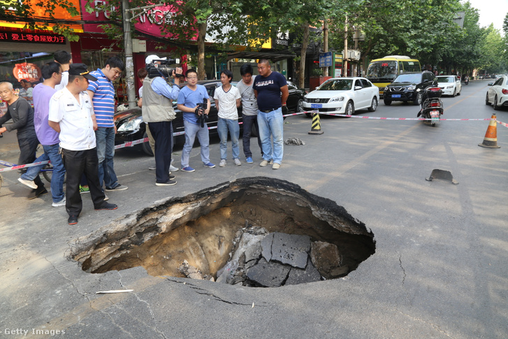 A lakosok egy mély gödröt néznek, amelyet az út süllyedése okozott a kínai Zhengzhou Henan tartományban 2015-ben