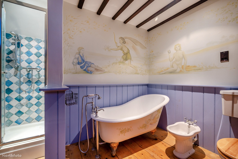 A hozzá tartozó fürdőszobában a lila szín dominál, a kád felett a falat festés díszíti, illetve zuhanyzó is található a helyiségben,