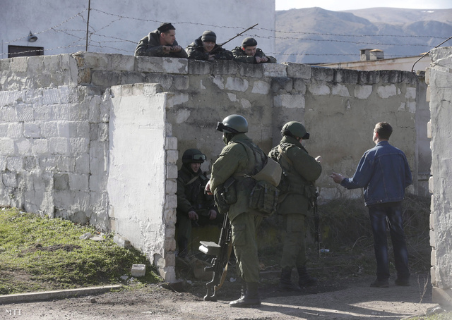 Ukrán katonák (fent) és feltehetően orosz katonák beszélgetnek egy ukrán katonai létesítmény kerítésénél Szimferopolban