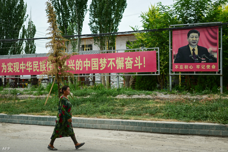 Egy nő Hszi Csin-ping plakátja előtt Kínában