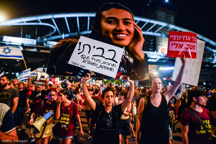 Tüntetők a megmentett izraeli női túsz, Noa Argamani fényképét ábrázoló plakátot tartanak, amelyen ez áll: „Otthon!” 2024. június 8-án Tel-Avivban, Izraelben