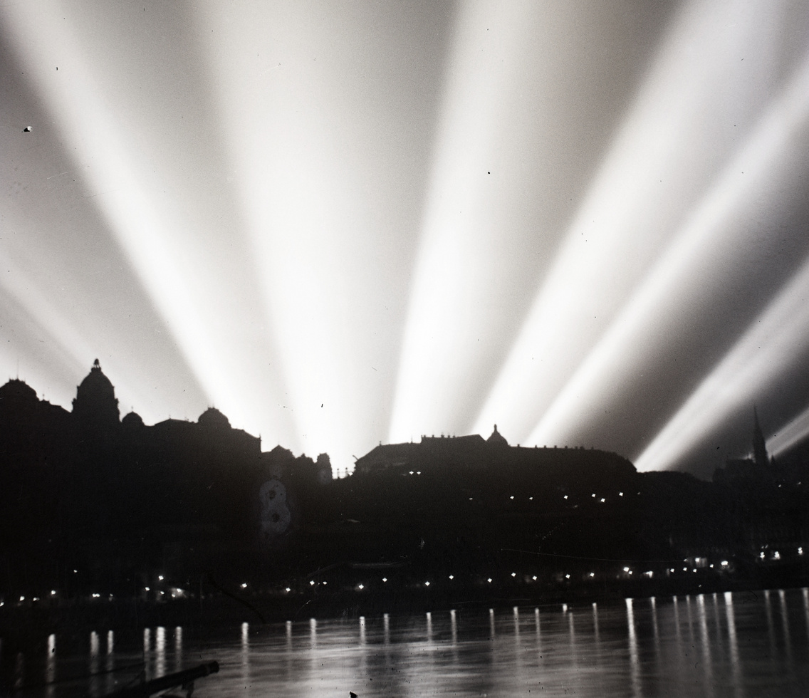 A Vár mögött a Vérmezőn felállított légvédelmi reflektorok fénye látható. A felvétel a pesti Duna-partról készült, 1937