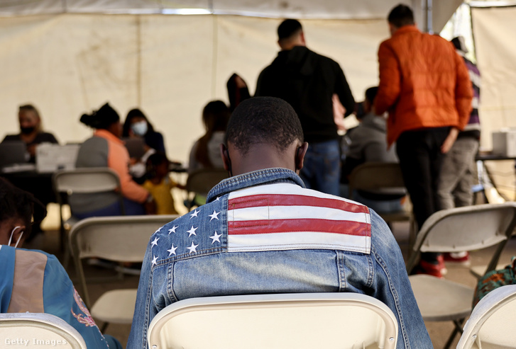 Egy ghánai bevándorló amerikai zászlós kabátot visel a határőrség őrizetéből kiengedett menedékkérők számára fenntartott átmeneti központban 2023. május 12-én az arizonai Somertonban