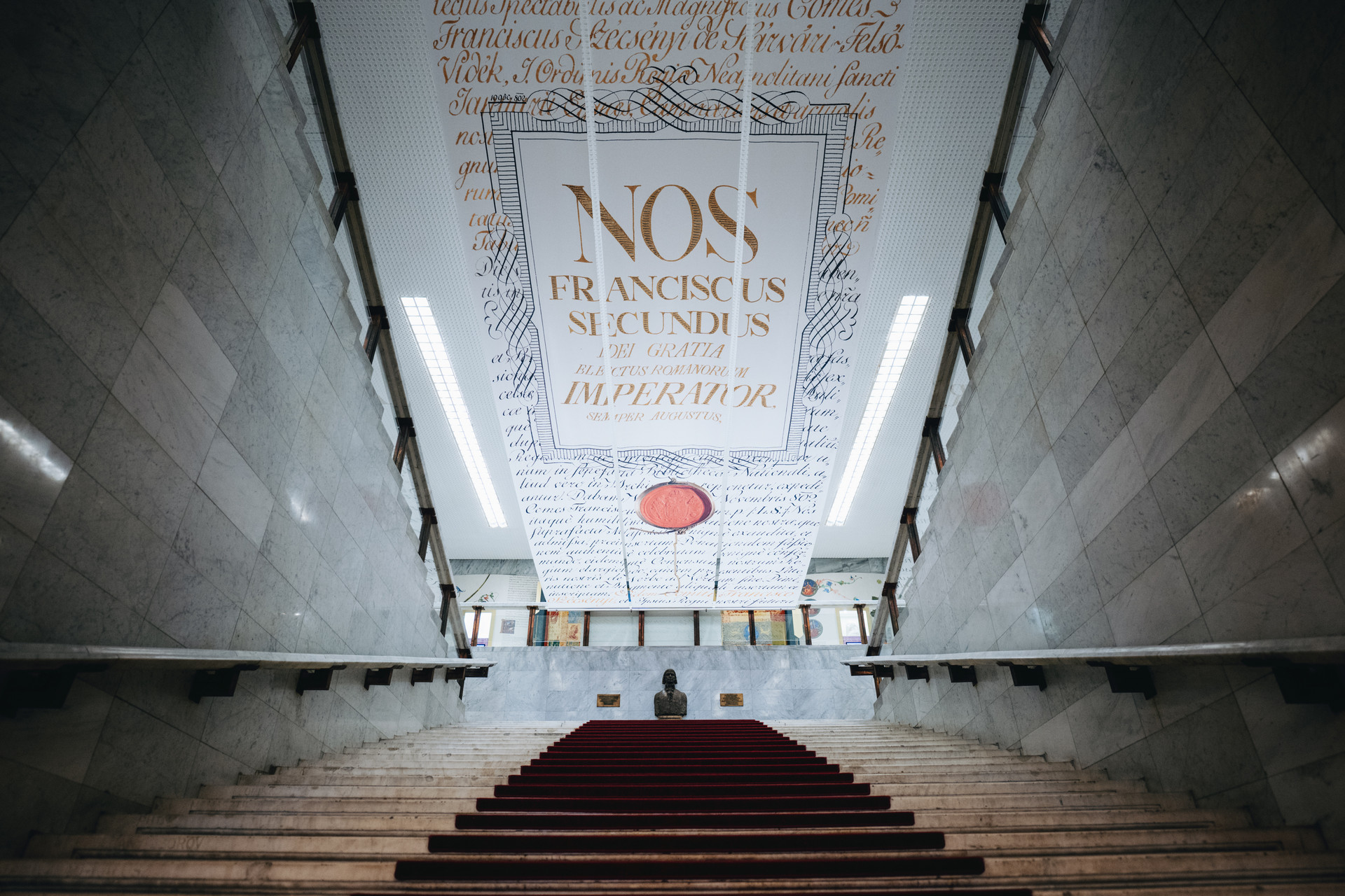 Az MNMKK Országos Széchényi Könyvtár Alapítók terébe vezető lépcsősora Széchényi Ferenc mellszobrával, felette pedig a könyvtár alapító okiratának másolatával