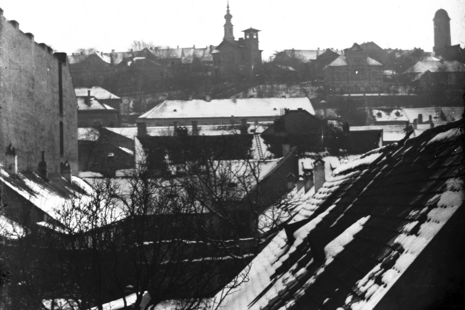 1905 telén a vízivárosi háztetők fehérbe burkolództak, fenn a budai Várban a Budavári Evangélikus templom és Mária Magdolna-templom tornya látszik.
