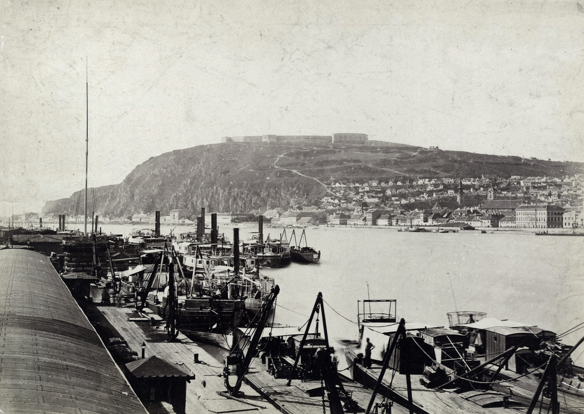 Teherhajó-kikötő és raktárai a pesti alsó rakparton a Széchenyi lánchídról nézve. Szemben a Gellért-hegy. A felvétel 1880 körül készült