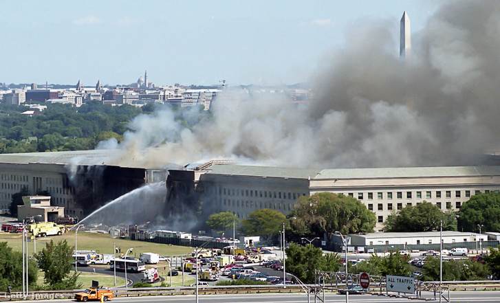A Pentagon nyugati oldalát tűzoltó tömlőkkel locsolják, miközben az épület továbbra is lángokban áll, a háttérben Washington látképével. A felvétel az arlingtoni James River House lakóépület tetejéről készült 2001. szeptember 11-én