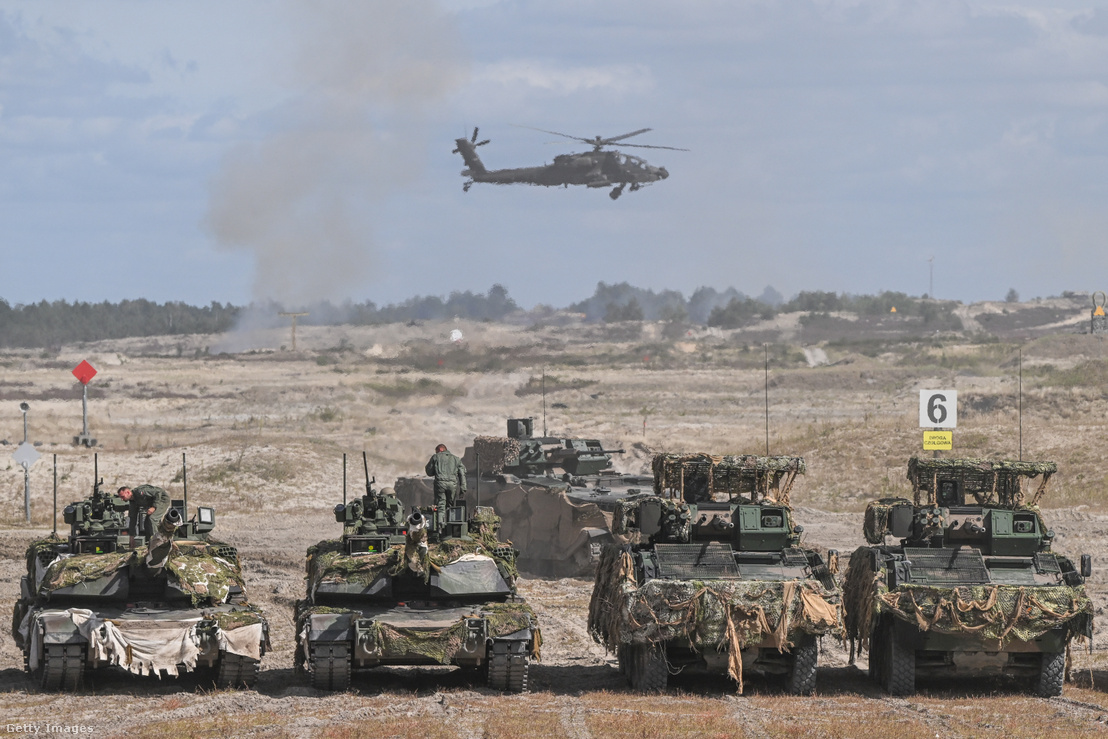 Illusztrációnkon egy Boeing AH–64 Apache harci helikopter látható M1A1 Abrams harckocsik és KTO Rosomak páncélozott járművek felett a lengyelországi Nowa Dębában 2026. szeptember 7-én