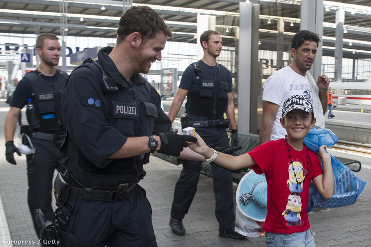Egy menekült kisfiú cukrot ad a német rendőrnek a müncheni pályaudvaron.